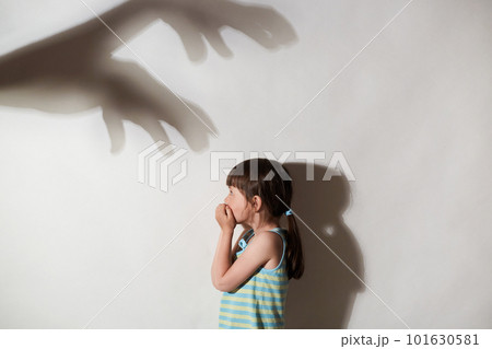 Profile of female kid frightened by the shadows of hands of demons, scared little girl suffering from sciophobia and phantoms, fear of shadows, isolated over gray background. 101630581
