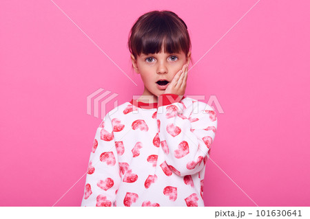 Little cute preschool girl looking at camera with her mouth open, sees something shocking, covers her cheek with her palm, wearing casual clothing, isolated over pink background. Little cute preschool girl looking at camera with her mouth open, sees something shocking, covers her cheek with her palm, wearing casual clothing, isolated over pink background. 101630641