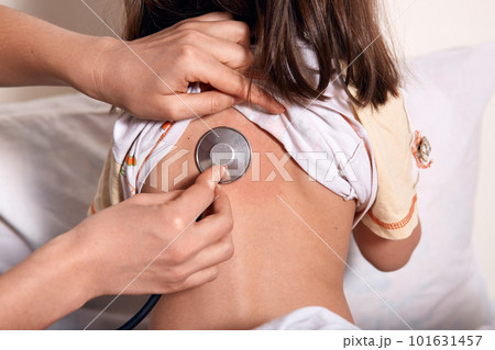 Close up portrait of pediatrician with patient child at clinic., dark haired female posing backwards, wearing pajama, doctor examines kids lungs. Diagnostic, healthcare, medical service concept. 101631457