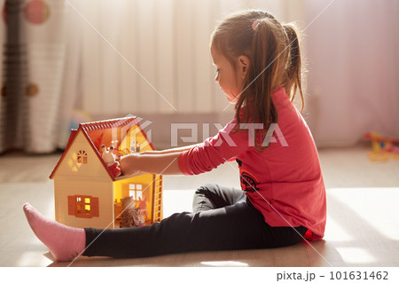 Little girl playing with her doll house. Child sitting on floor in her bedroom, female kid plays in her room at home or kindergarten. Toddler kid with toy house. Children entertainment concept. 101631462