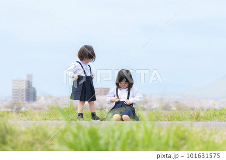 春の河川敷で遊ぶ幼稚園の制服を着た姉妹 101631575