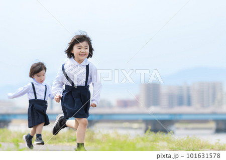 春の河川敷を走る幼稚園の制服を着た姉妹 101631578