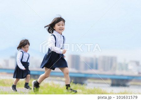 春の河川敷を走る幼稚園の制服を着た姉妹 101631579