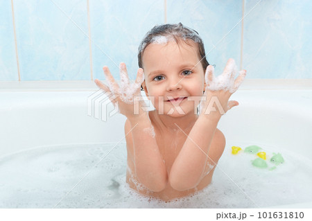 Small adorable child has funny expression, taking bath with plesure, plaing in hot water and shows hands with foam, poses in bathroom against blue wall. Playful little kid glad to be photographed. Small adorable child has funny expression, taking bath with plesure, plaing in hot water and shows hands with foam, poses in bathroom against blue wall. Playful little kid glad to be photographed. 101631810