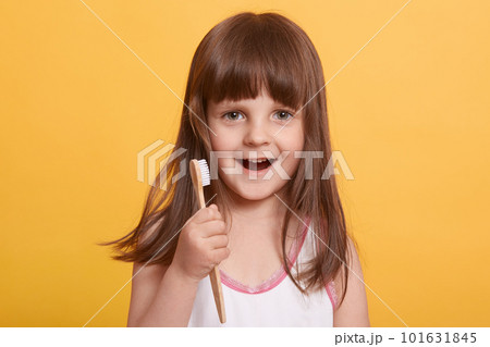 Studio shot of beautiful happy surprised dark haired little girl in bathroom, brushing teeth with excited facial expression, posing isolated over yellow background. Childhood, daily procedures concept 101631845