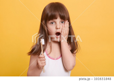 Studio shot of emotional impressed little girl opening mouth widely, having surprised facial expression, putting hand on cheeck, holding toothbrush, looking directly at camera. Hygiene concept. Studio shot of emotional impressed little girl opening mouth widely, having surprised facial expression, putting hand on cheeck, holding toothbrush, looking directly at camera. Hygiene concept. 101631848