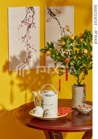 Front view of tea set, kumquat tree and lucky money on wood table on yellow background. Table with beautiful decorations for Chinese New Year celebration in room Front view of tea set, kumquat tree and lucky money on wood table on yellow background. Table with beautiful decorations for Chinese New Year celebration in room 101632000