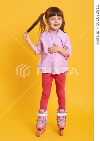 Smiling happy female posing isolated over yellow background, wearing leggins and casual shirt, kid touching her ponytail, look sat camera, child roller skating. 101632911