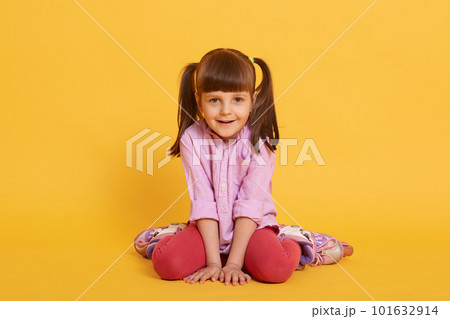 Cute girl sits in rollers in shirt and leggins and smiles, having two ponytail, looks happy, posing isolated over yellow background, funny female child. 101632914