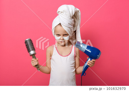 Girl with comb and hair dry looking directly at camera with shy facial expression, has patches under eyes, having white towel on her head, posing against pink background. 101632970