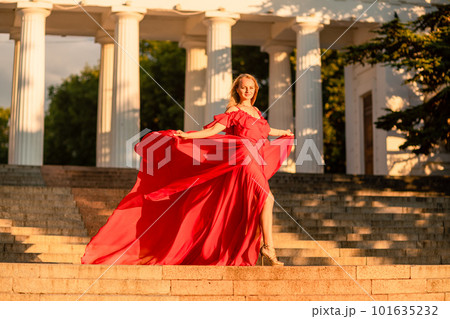 A woman in a long red dress against the backdrop of sunrise, bright golden light of the sun's rays. The concept of femininity, harmony. 101635232