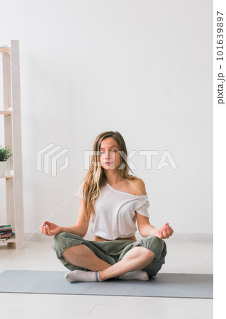 Young healthy beautiful woman practicing yoga at home sitting in lotus pose on yoga mat meditating smiling relaxed with closed eyes - Mindfulness meditation concept 101639897
