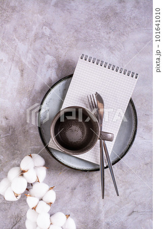 Empty ceramic mug, cutlery and notebook on a plate on a gray background top and vertical view Empty ceramic mug, cutlery and notebook on a plate on a gray background top and vertical view 101641010
