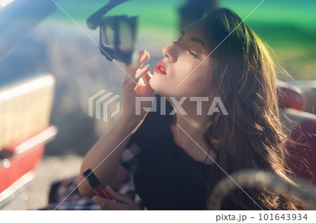 successful business lady driving a car in sunglasses paints her lips with lipstick while looking in the mirror. 101643934