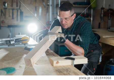 Carpenter measures a wooden board while working in a workshop.  101644068