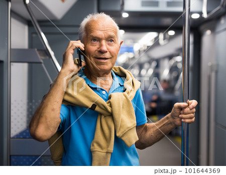 Positive elderly passenger talking on mobile phone in subway car 101644369