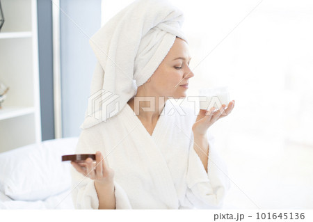 Lady after shower holding facial cream in hand at home Lady after shower holding facial cream in hand at home 101645136