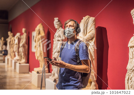 Portrait of contemporary man looking at sculptures and listening to audio guide at museum exhibition 101647022