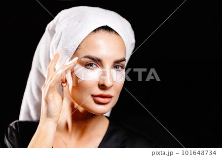 Young beautiful woman in white towel and robe taking on eye patch looking in camera. 101648734