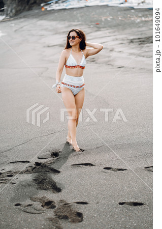 Brunette girl walking on the black sand beach wearing a cute bathingsuit in Bali Indonesia 101649094