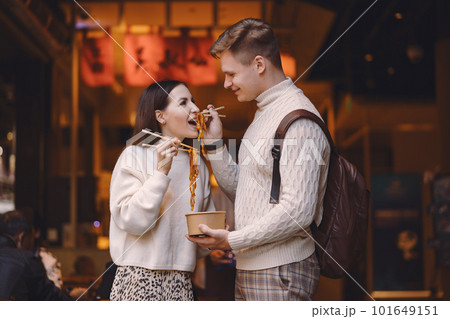 newlywed couple eating noodles with chopsticks in Shanghai outside a food market near Yuyuan. Couple eating authentic local food. husband and wife eating chinese food outisde of a food hall newlywed couple eating noodles with chopsticks in Shanghai outside a food market near Yuyuan. Couple eating authentic local food. husband and wife eating chinese food outisde of a food hall 101649151
