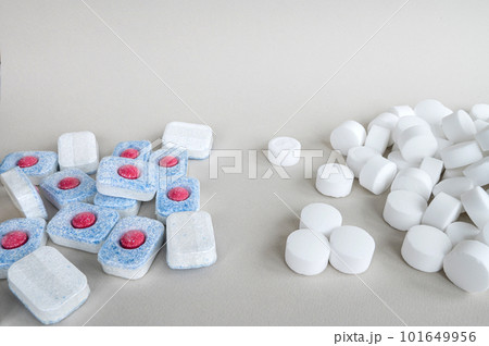 White pressed salt tablets and colored dishwasher capsules close-up. Place for text 101649956
