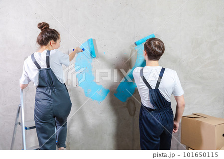 Couple in new home during repair works painting wall together. Happy family holding paint roller painting wall with blue color paint in new house. Home renovation DIY renew home concept Couple in new home during repair works painting wall together. Happy family holding paint roller painting wall with blue color paint in new house. Home renovation DIY renew home concept 101650115