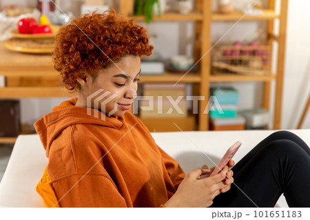 African girl holding smartphone touch screen typing scroll page at home. Woman with cell phone surfing internet using social media apps playing game. Shopping online Internet news cellphone addiction 101651183