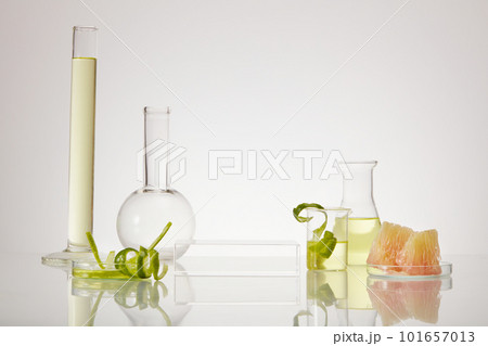 Front view of scientific glassware with essential oil inside of pink pomelo (Citrus maxima) extract. Empty transparent podium to promote product. 101657013