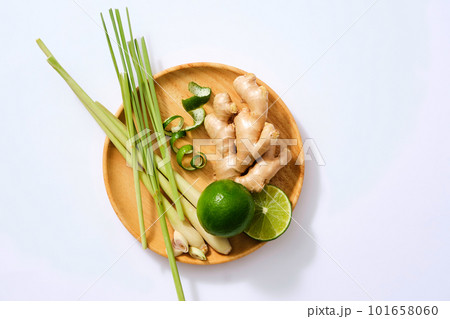 Scene for advertising with fresh lemongrass, lemon and ginger root on wooden dish, isolated on white background. These are healthy foods and spices in cooking. Top view, flat lay. Scene for advertising with fresh lemongrass, lemon and ginger root on wooden dish, isolated on white background. These are healthy foods and spices in cooking. Top view, flat lay. 101658060