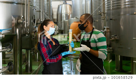 Man and a woman in protective masks analyze the white wine in beaker Man and a woman in protective masks analyze the white wine in beaker 101658529