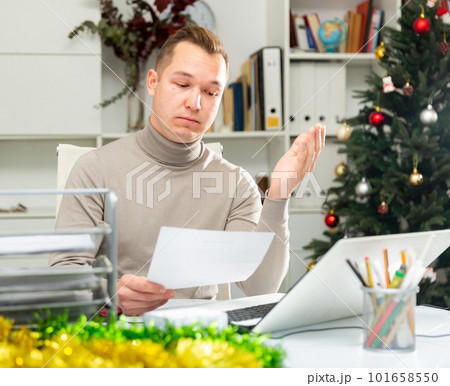 Disappointed office worker doing his paperwork during Christmastime Disappointed office worker doing his paperwork during Christmastime 101658550