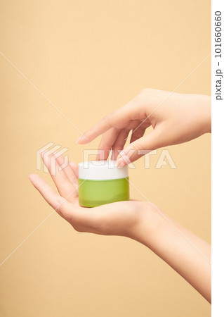 Scene of a green glass jar in a woman's hand. The other hand is preparing to open the lid. Cosmetic product branding mockup. Daily skincare and body care routine. Front view, space for design. 101660660