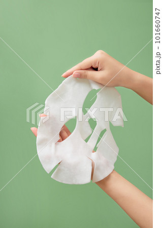 A white skincare mask is held on hand model against a light green background. Skincare mask treatment for face. Beauty product A white skincare mask is held on hand model against a light green background. Skincare mask treatment for face. Beauty product 101660747