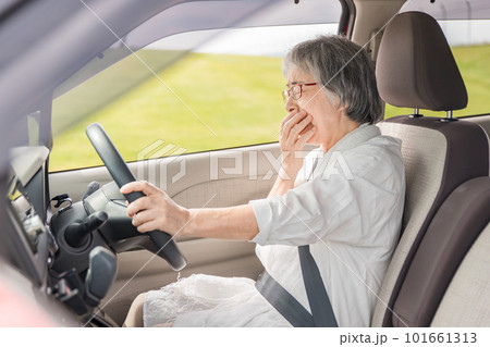 自動車の運転中に眠気を感じてあくびをする高齢者・シニア女性 101661313