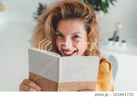 Waist up portrait of a smiling woman hiding behind her notebook  101661720