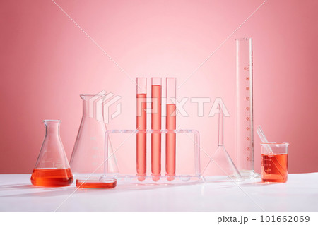 Front view of assortment of glass containers for laboratory, containing pink liquid and transparent empty podiums on pink background. Space for product presentation 101662069