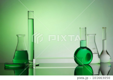 Front view of transparent empty podium, laboratory equipment - test tube, boiling flask, erlenmeyer flask and petri dish on green gradient background. Space for display product. 101663050