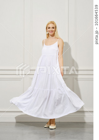 A happy woman in a waving white sundress stands elegantly indoors 101664539