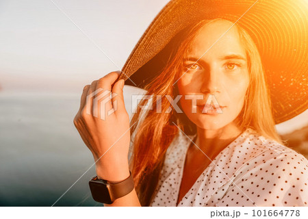 Portrait of happy young woman wearing summer black hat with large brim at beach on sunset. Closeup face of attractive girl with black straw hat. Happy young woman smiling and looking at camera at sea. Portrait of happy young woman wearing summer black hat with large brim at beach on sunset. Closeup face of attractive girl with black straw hat. Happy young woman smiling and looking at camera at sea. 101664778