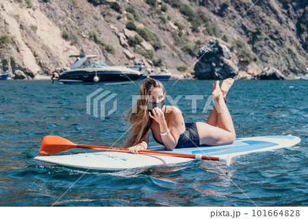 Woman sea sup. Close up portrait of happy young caucasian woman with long hair looking at camera and smiling. Cute woman portrait in bikini posing on sup board in the sea Woman sea sup. Close up portrait of happy young caucasian woman with long hair looking at camera and smiling. Cute woman portrait in bikini posing on sup board in the sea 101664828