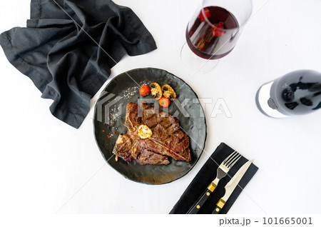 Bone-in beef steak on a black plate with a glass of wine 101665001