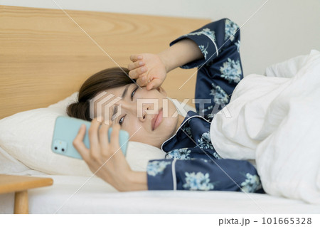 ベッドに寝ながらスマホを見て顔をしかめるミドルの女性 101665328