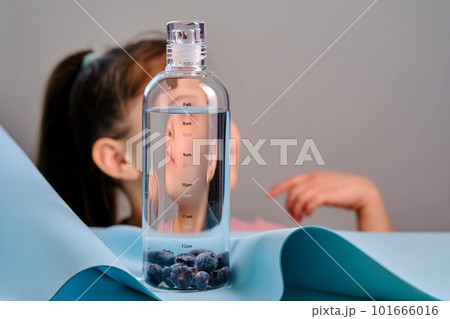 The girl looks into a glass bottle of pure water. The girl looks into a glass bottle of pure water. 101666016