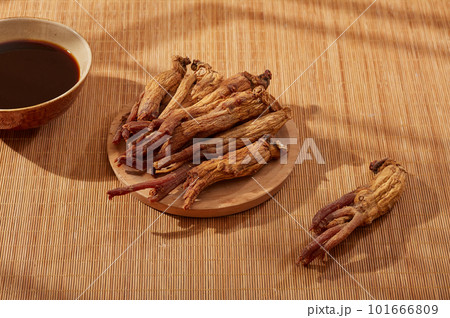 Red ginseng displayed on wooden dish with a bowl of medicine. Red ginseng (Panax ginseng) helps strengthen the body's immune function, support the symptoms of fatigue and body weakness 101666809