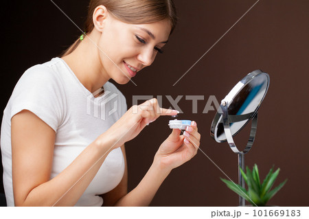 A young woman is putting on contact lenses in front of the mirror. A young woman is putting on contact lenses in front of the mirror. 101669183