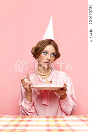 Beautiful young girl with bright makeup, with cigarette, holding birthday cake against pink studio background. Celebration 101670780