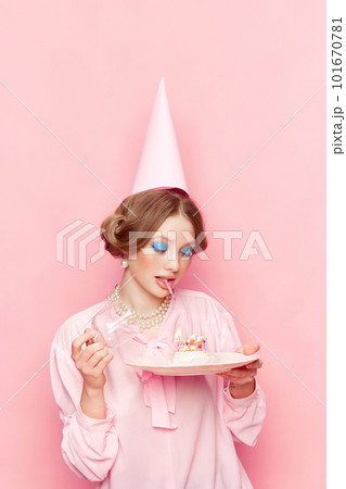 Stylish, beautiful, young girl with makeup opening her birthday cake against pink studio background. Make your wish 101670781