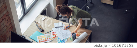 High angle view of interior designer or architect in casual wear with messy hairdo working with color samples and blueprint for new project, standing in her office 101671558