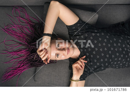 Portrait of pretty casually dressed caucasian young woman with dreadlocks looking into camera and lying on the sofa. Portrait of pretty casually dressed caucasian young woman with dreadlocks looking into camera and lying on the sofa. 101671786